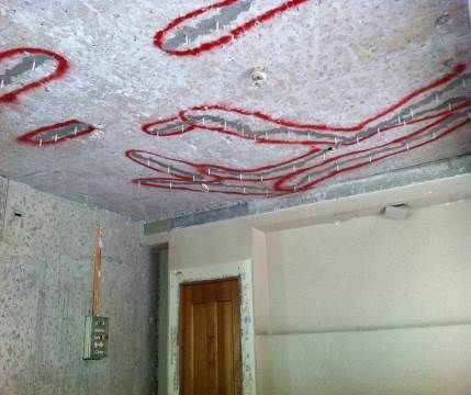 Habitación con techo sin terminar, bucles de cableado rojo, una puerta y un panel eléctrico montado en la pared.