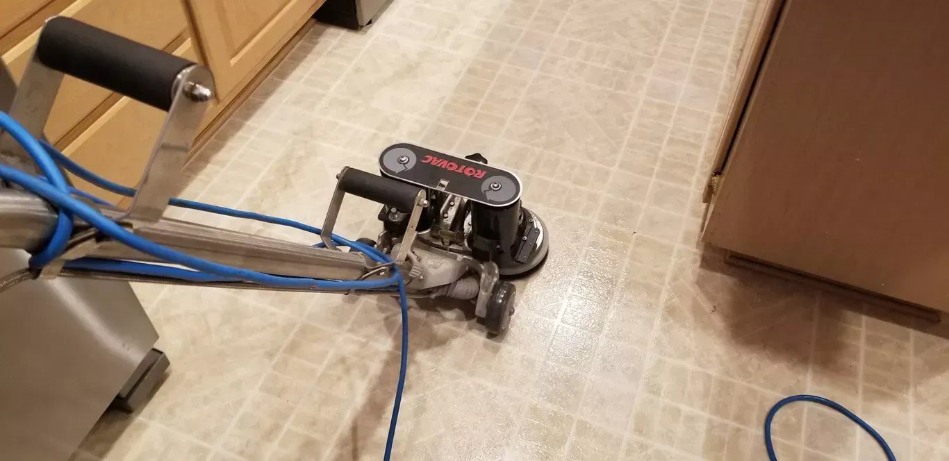 A machine is being used to clean a tile floor in a kitchen.
