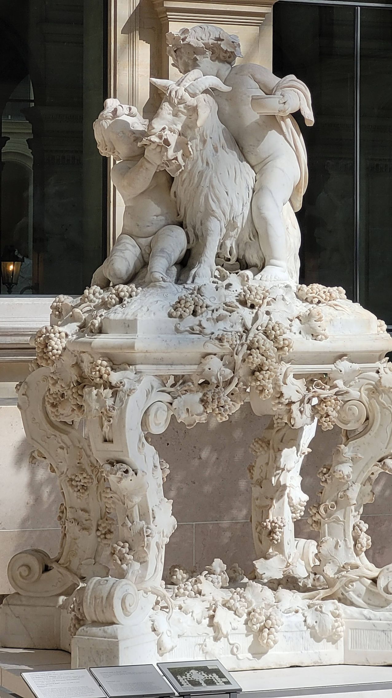 Figure scolpite di bambini e una capra su un piedistallo decorativo.