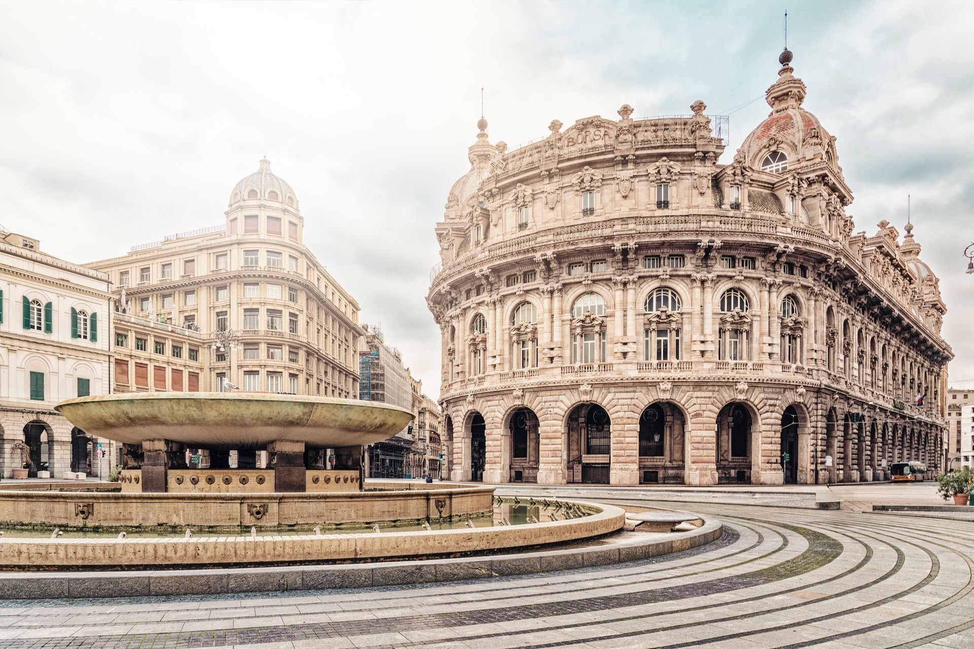 Una piazza di Genova, in Italia, con edifici in pietra decorati, una fontana e un cielo nuvoloso.