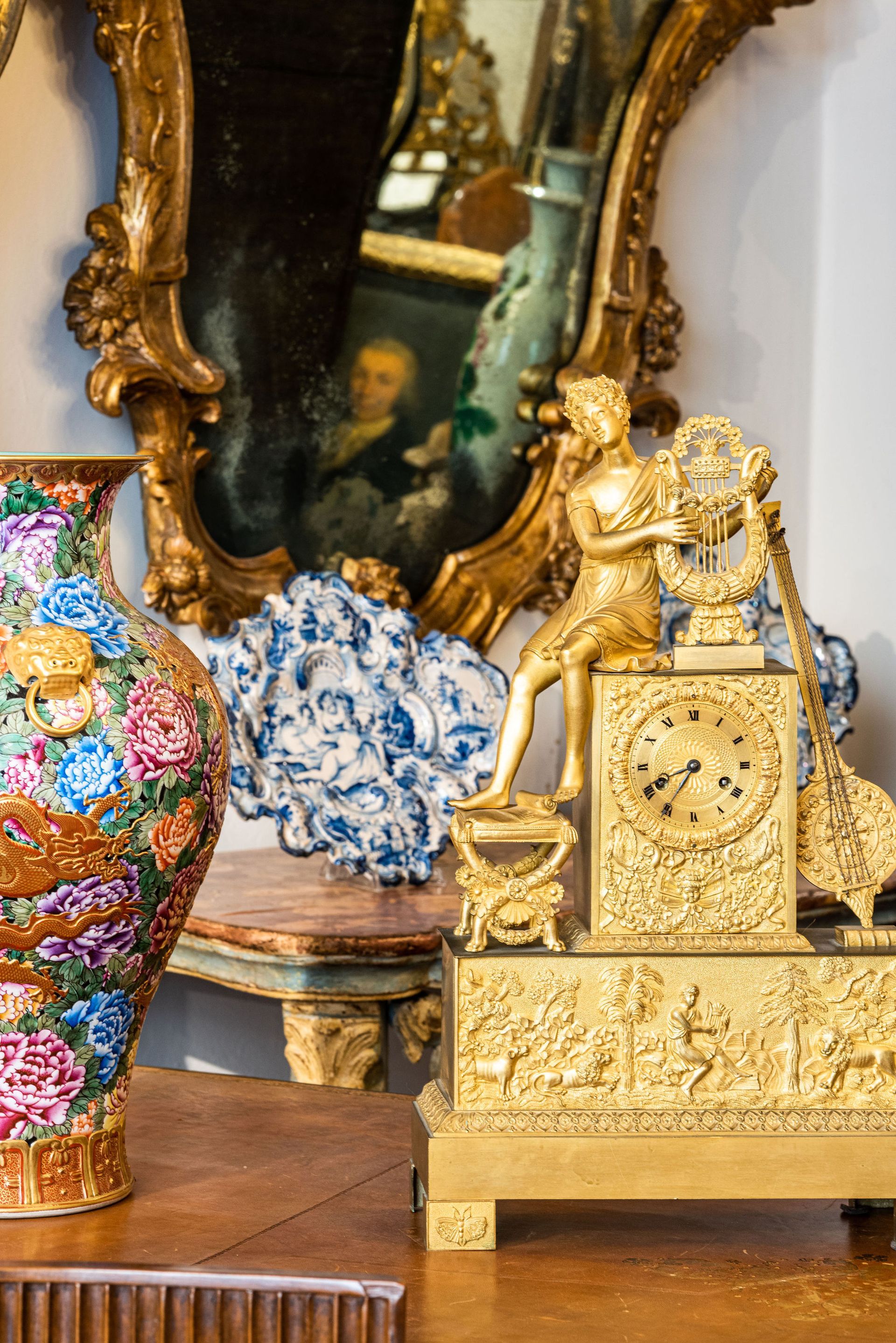 Orologio dorato decorato con una figura, vaso con motivo floreale e specchio antico.