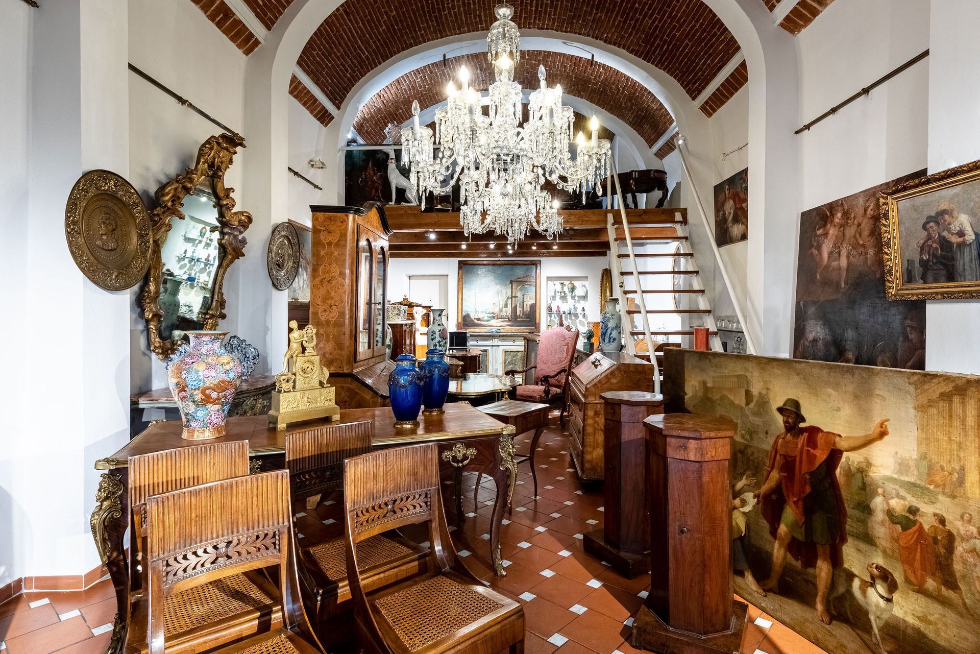Interno di un negozio di antiquariato con mobili, dipinti e un lampadario.