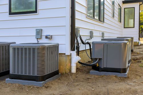 A row of air conditioners are sitting on the side of a house.
