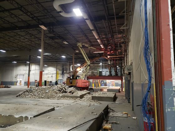 A large warehouse is being demolished with a bulldozer in the middle
