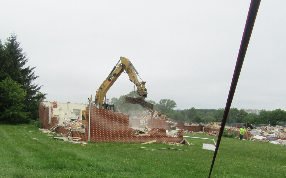 An excavator is demolishing a brick building in a field