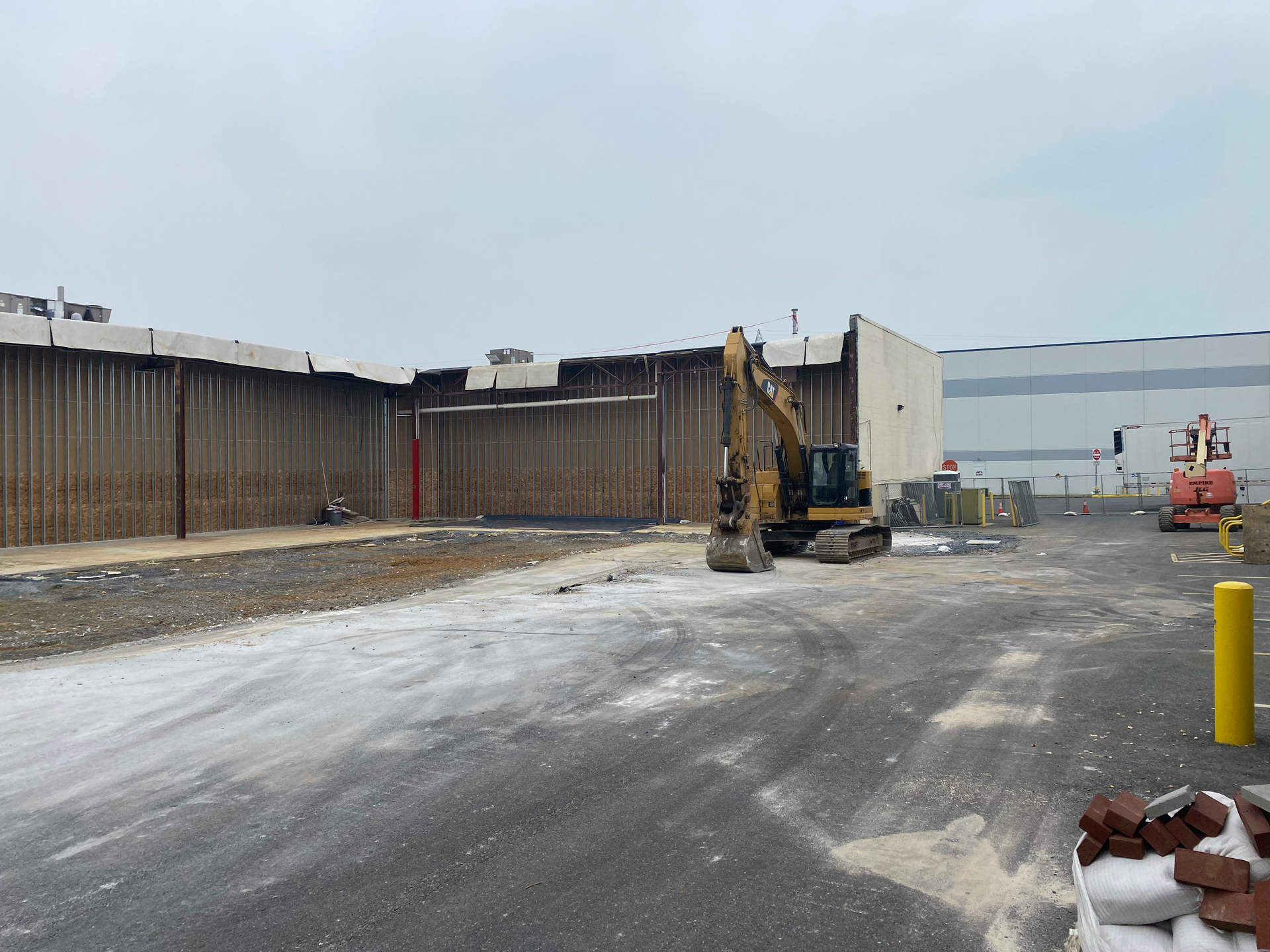A construction site with a large building in the background and a yellow pole in the foreground.