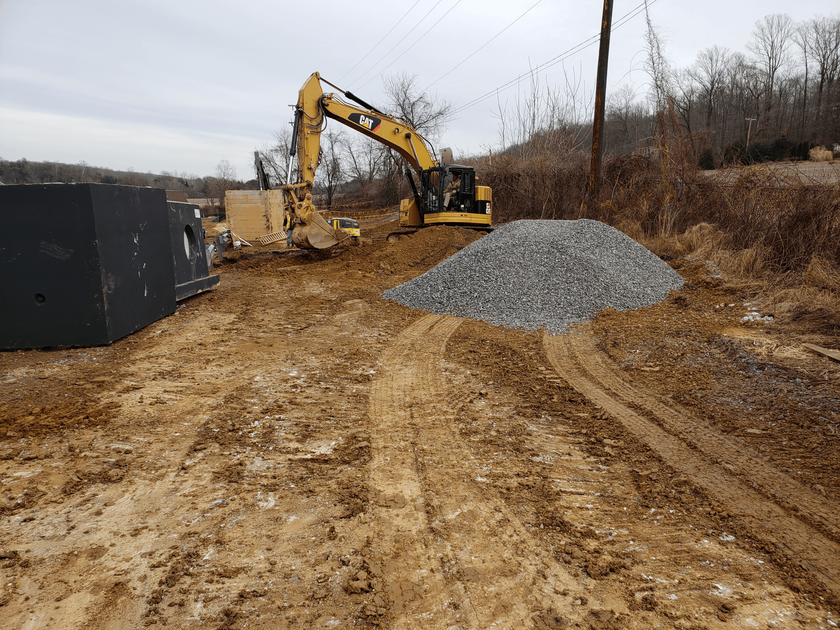 A yellow excavator is working on a dirt road next to a pile of gravel.