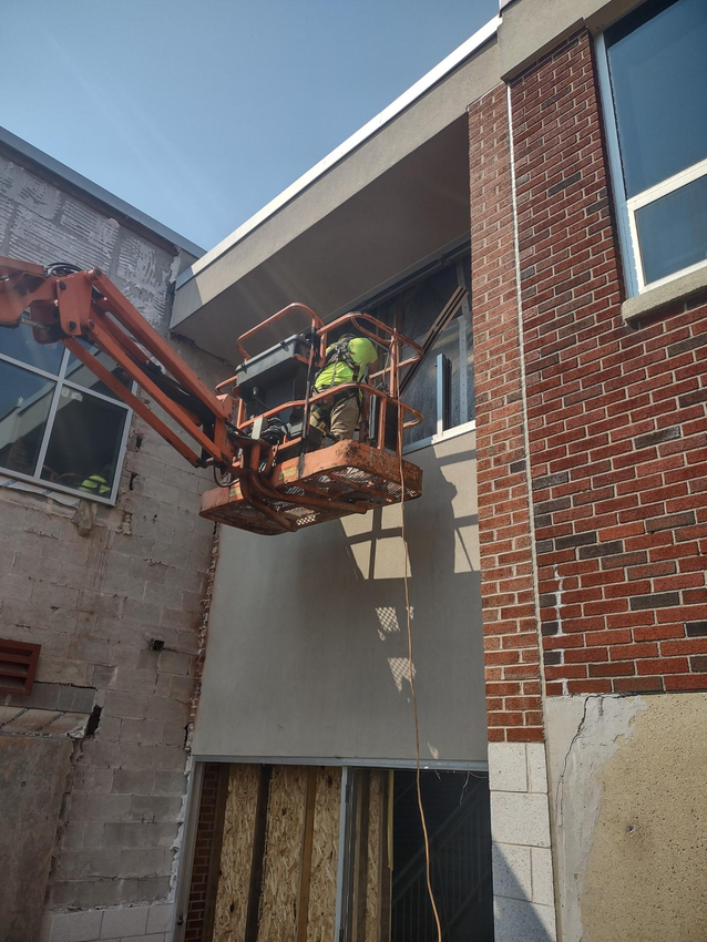 A man in a bucket is working on a brick building.
