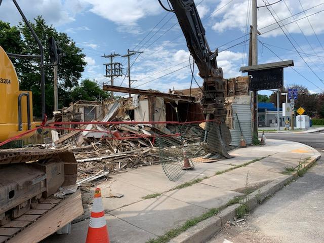 A yellow excavator is demolishing a building on the side of the road.