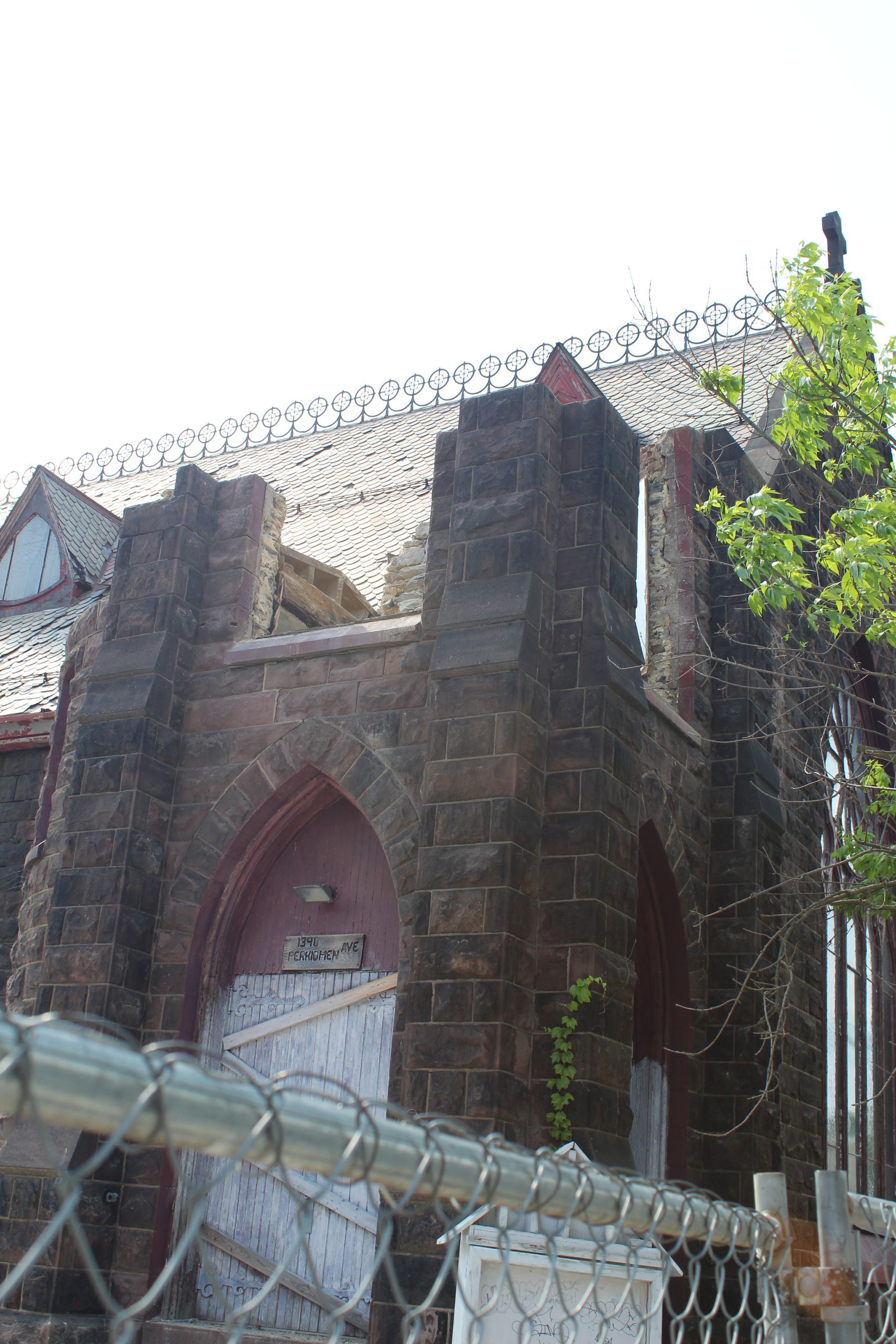 Stone church exterior with barbed wire on the roof, behind a chain-link fence.