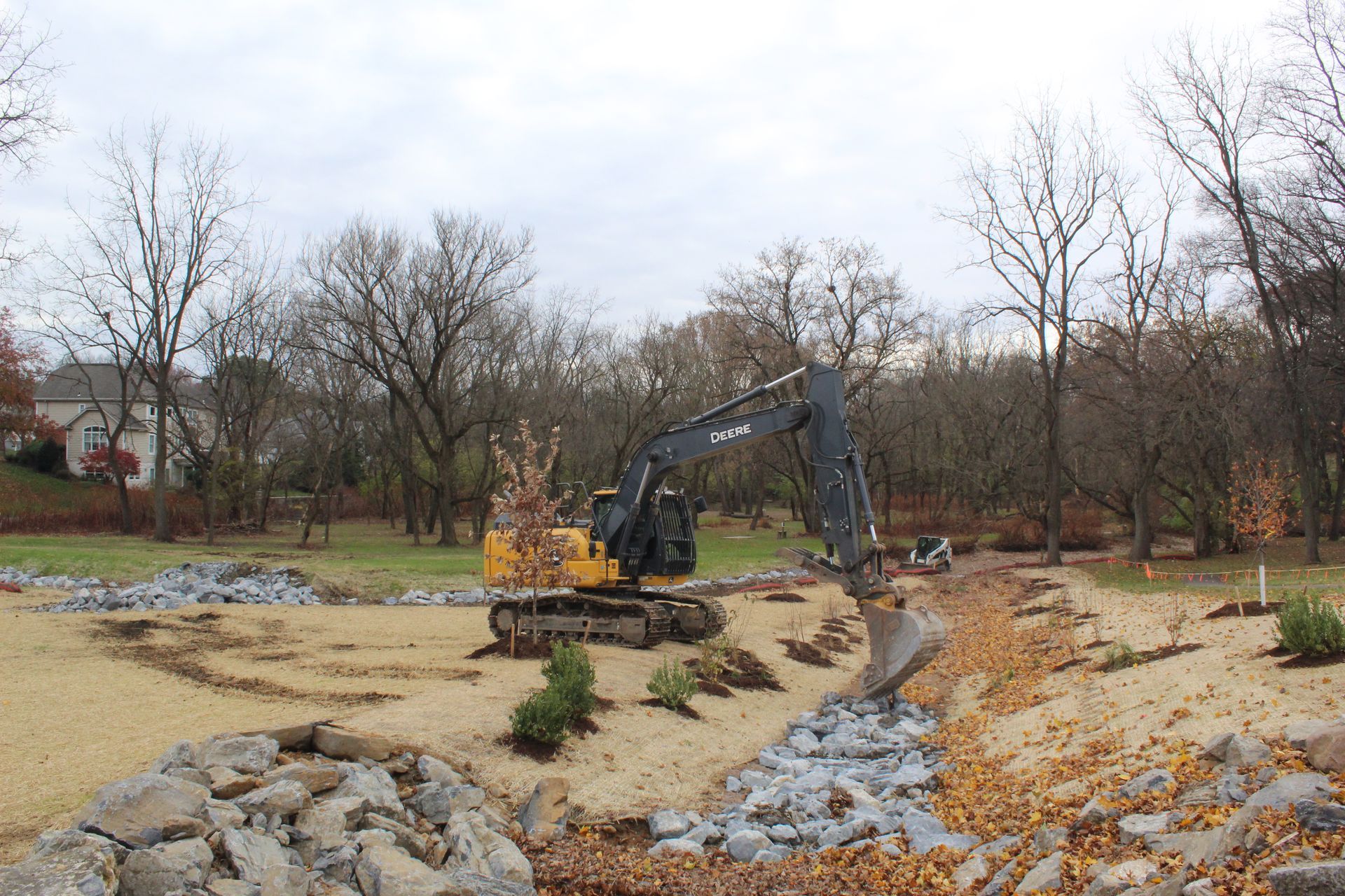 Excavator working on a stream bank, removing material, with trees in the background.