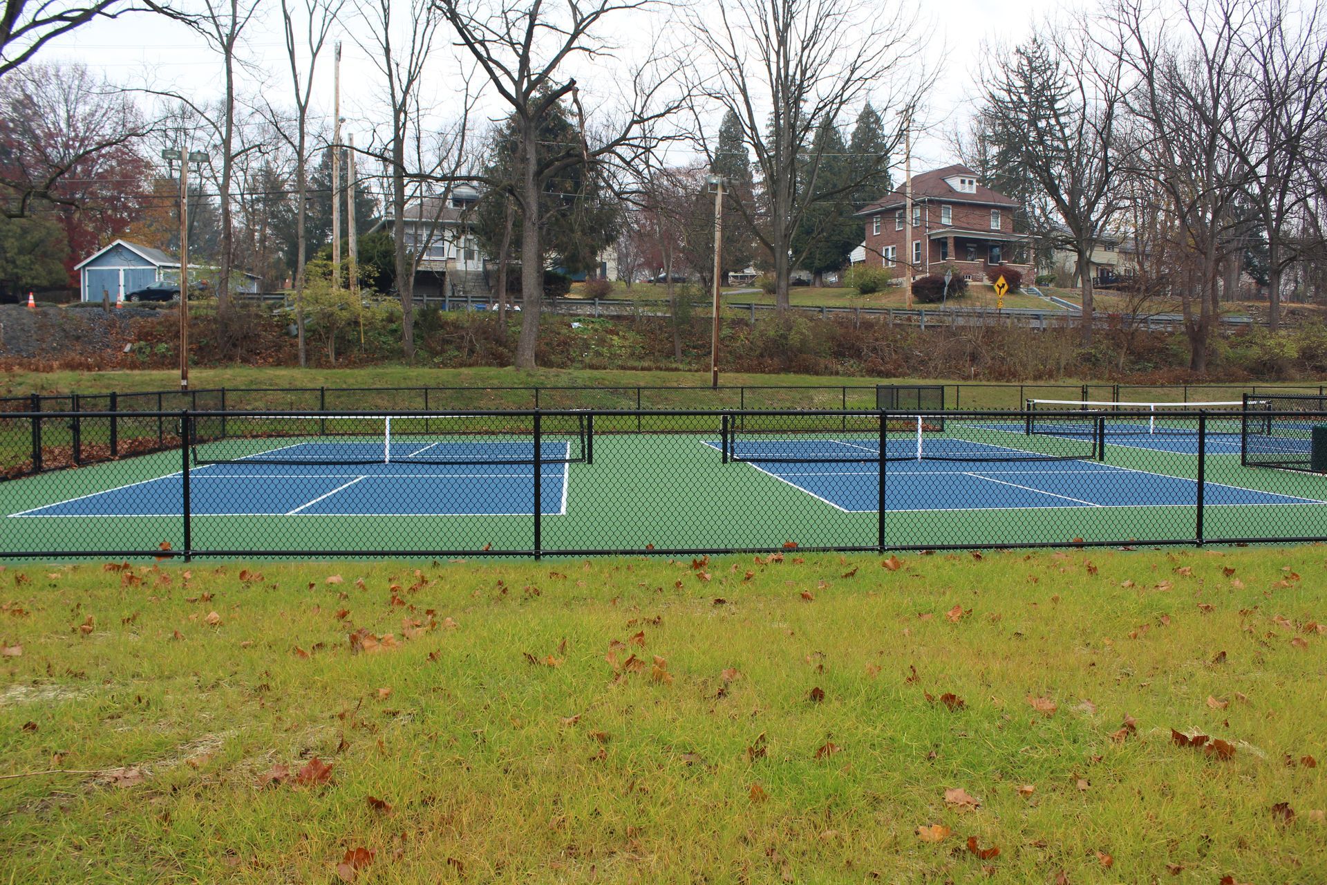 New pickleball courts behind a black fence, surrounded by grass. Empire Services performed the excavation and grading.
