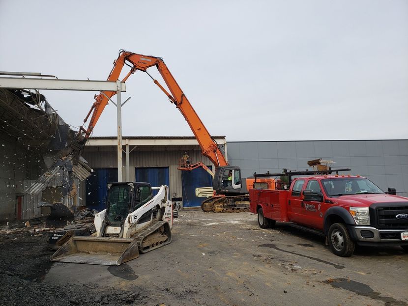 A red truck is parked next to a bulldozer in a parking lot.
