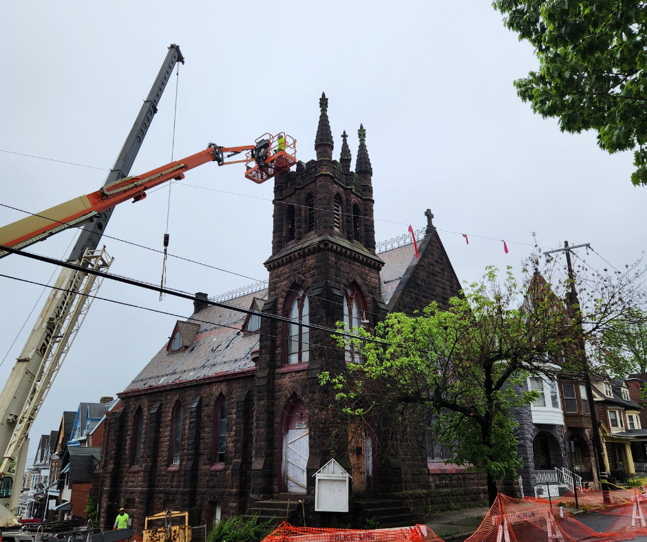 Crane with lift basket near brick church steeple with workers.  
