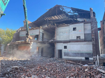 A large building is being demolished by a crane.