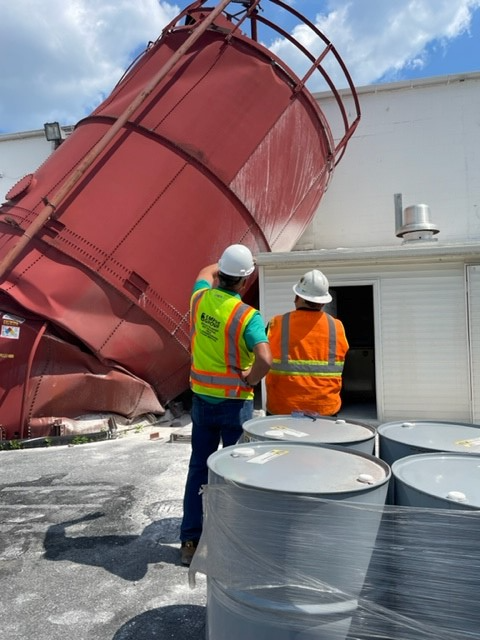 Two men wearing hard hats are standing in front of a large red silo
