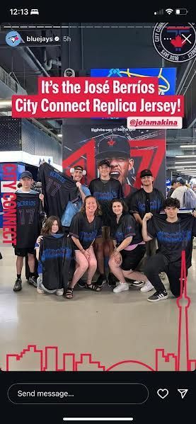 A group of fans poses in front of a Blue Jays poster, wearing dark José Berríos City Connect jerseys at a stadium.