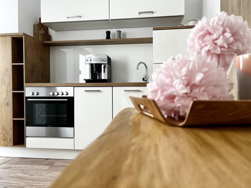 Moderne Küchenzeile der Ferienwohnung mit Backofen, Kaffeemaschine und dekorativen rosa Pompons im Vordergrund