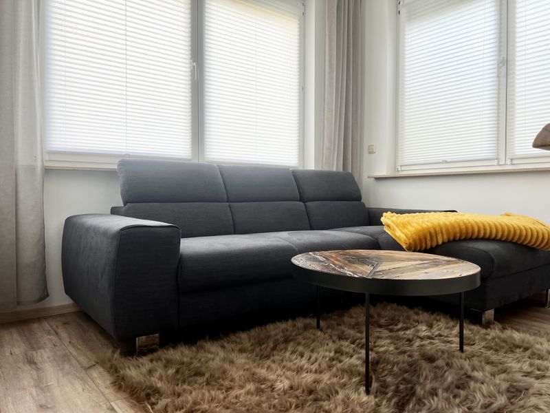 gemütliches dunkles Sofa im Wohnzimmer mit einer gelben Kuscheldecke und Couchtisch