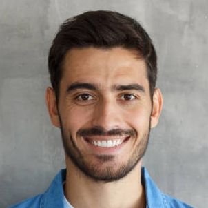 Smiling man with dark hair and beard in a blue shirt against a gray background