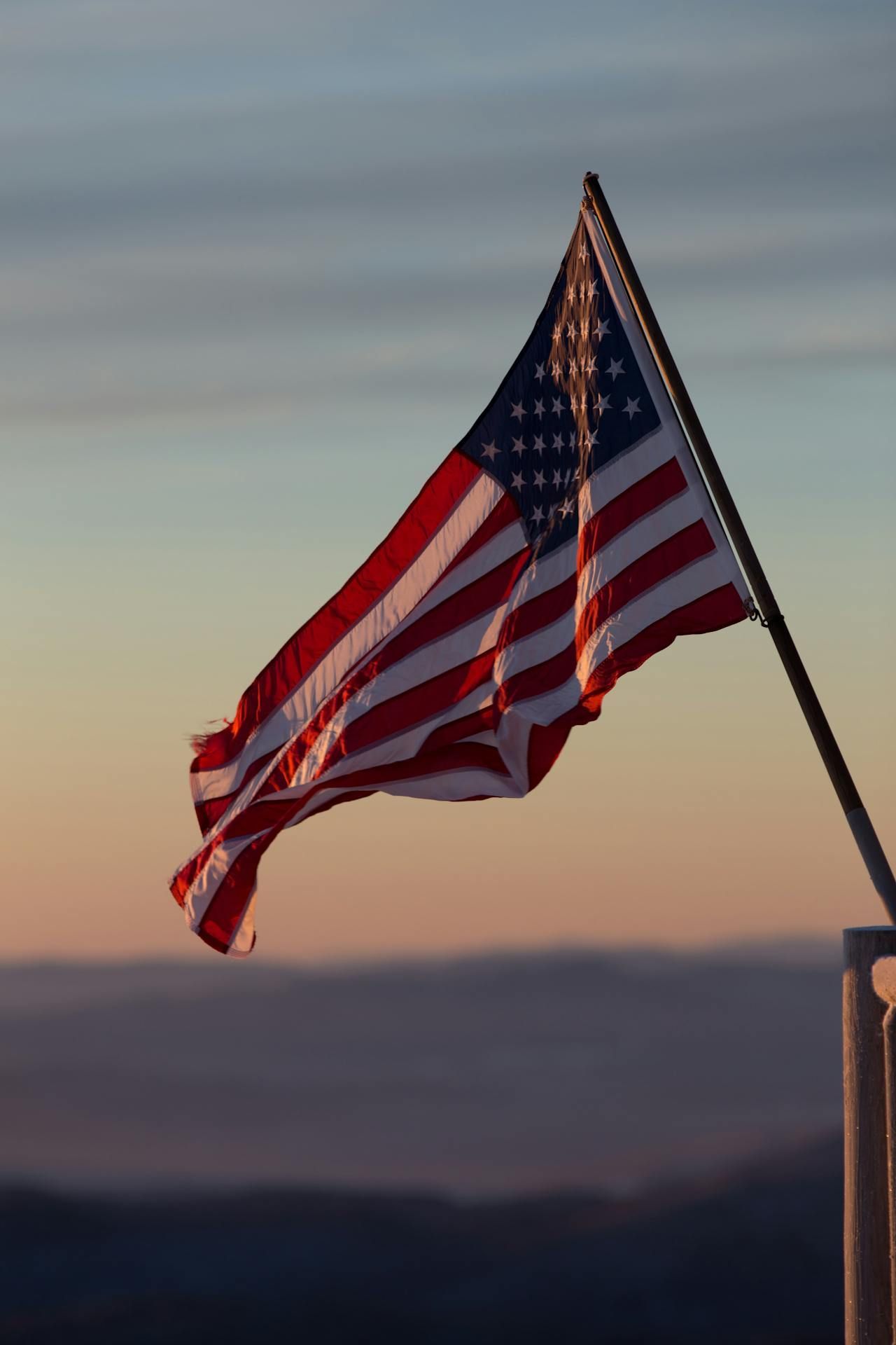 American flag waving in the wind against a blurred, colorful sky at sunset.