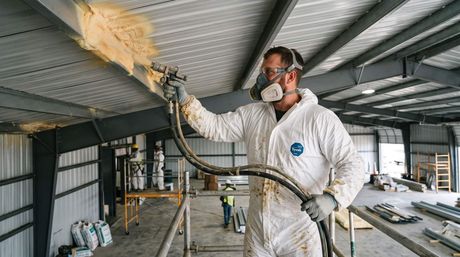Male spraying foam insulation under the roofing of a metal building