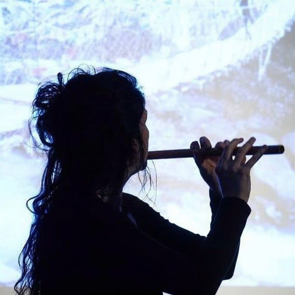 Silhouet van Jennette Roozeboom, fluitist, die speelt tegen een heldere, geprojecteerde achtergrond.