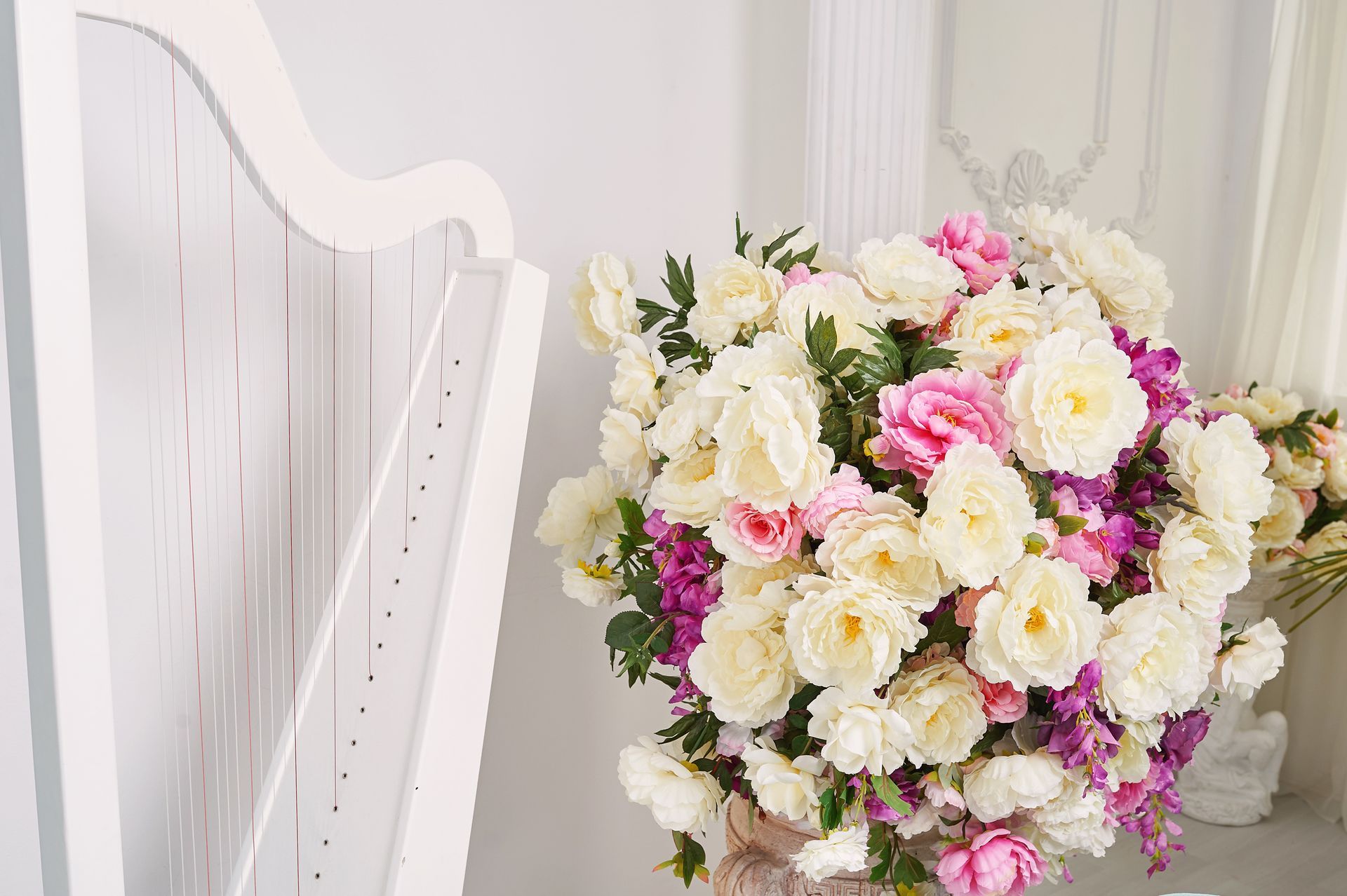 Witte harp naast een pastelkleurig bloemenboeket in een lichte kamer.
