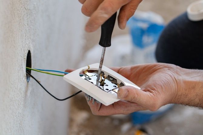 Hands wiring a white wall electrical outlet with a screwdriver