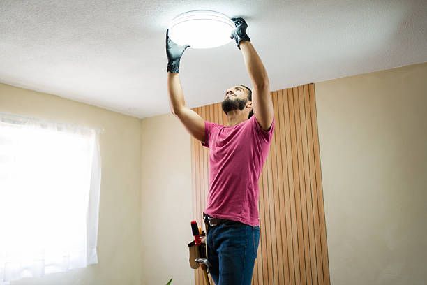 Person installing a ceiling light fixture in a room with beige walls and wood paneling