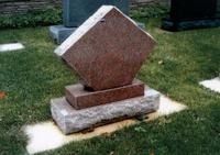 Small abstract stone sculpture on a lawn, with stacked rectangular bases and a tilted diamond-shaped top.