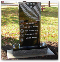 Black memorial plaque honoring county armed forces, with U.S. flag and military emblems on a stone base.