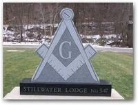 Masonic lodge sign with compass and square emblem, reading “Stillwater Lodge No. 54,” on a lawn.
