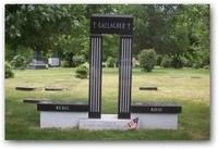 Black memorial bench and arch in a grassy cemetery, with a small flower at the base.