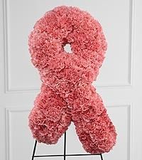 Pink ribbon-shaped floral arrangement on a stand against a white wall.