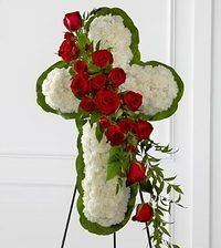 Cross-shaped white floral arrangement with red roses and green trim on a stand