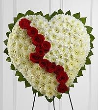 Heart-shaped white floral wreath with a diagonal red rose stripe on a stand