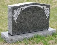 Gray granite headstone with decorative floral carvings on a grassy grave site