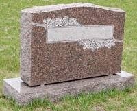 Pink granite gravestone on a concrete base in a grassy cemetery