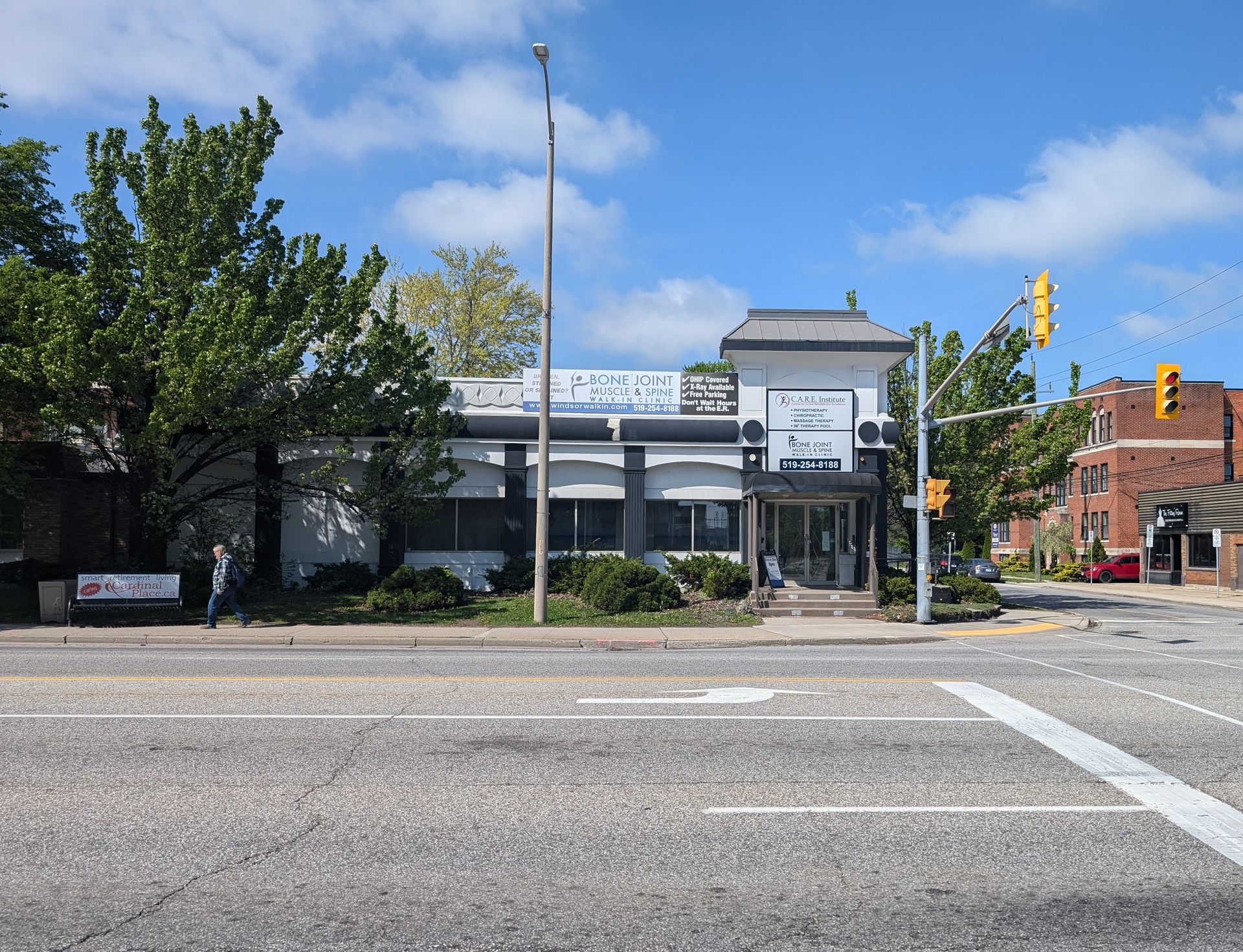 Street view of a storefront building with trees, traffic lights, and a blue sky.