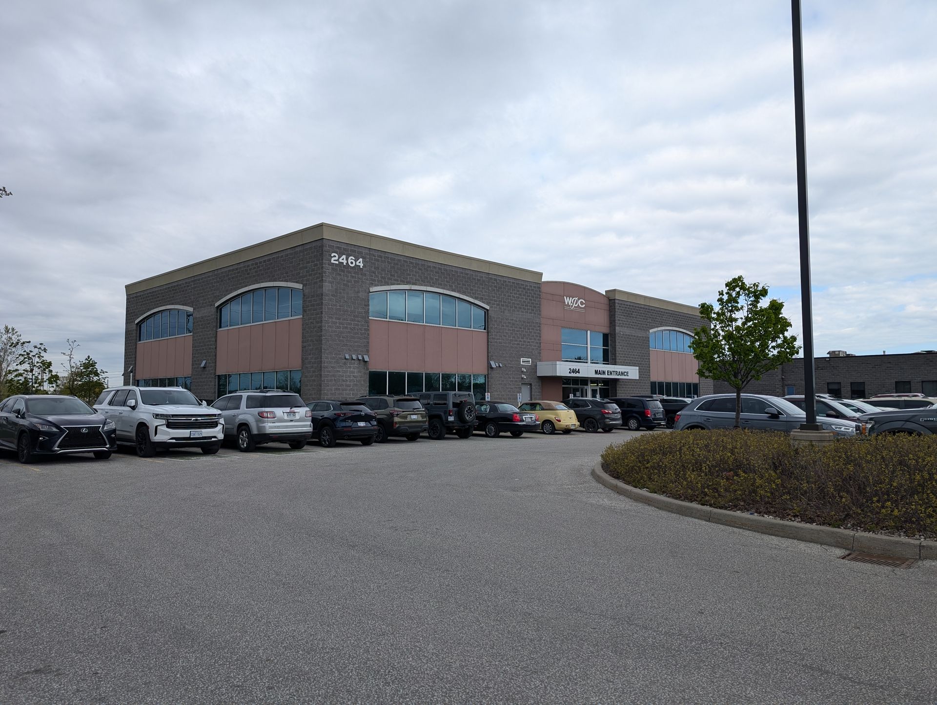 Large brick commercial building with parked cars in front under a cloudy sky