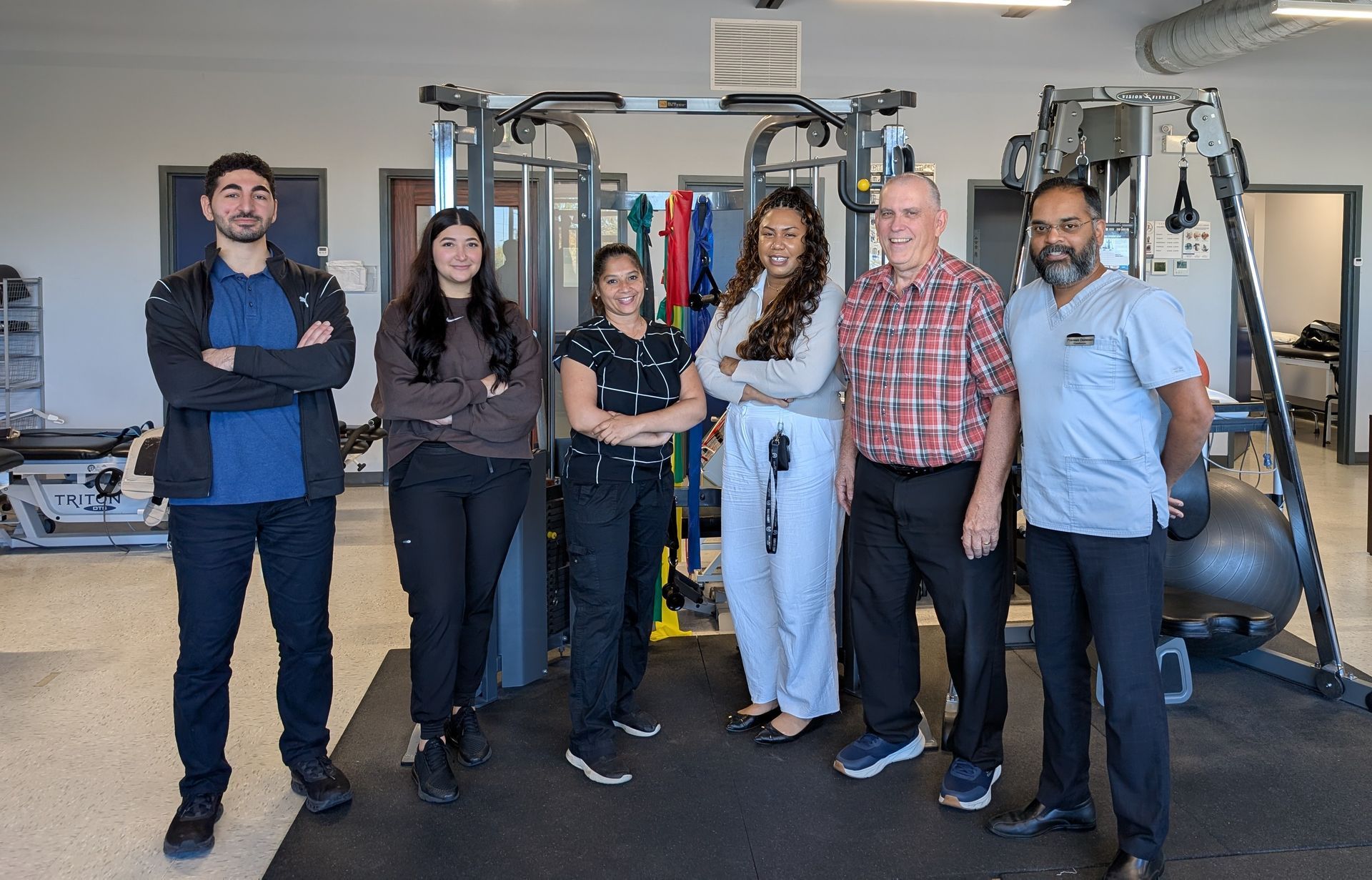 Group posing in a gym, standing in front of weight machines with exercise balls in the background.