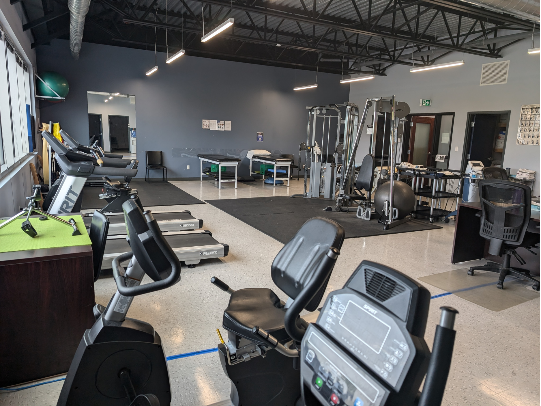 Gym interior with cardio machines, treadmills, weights, and black exercise equipment on a gray floor