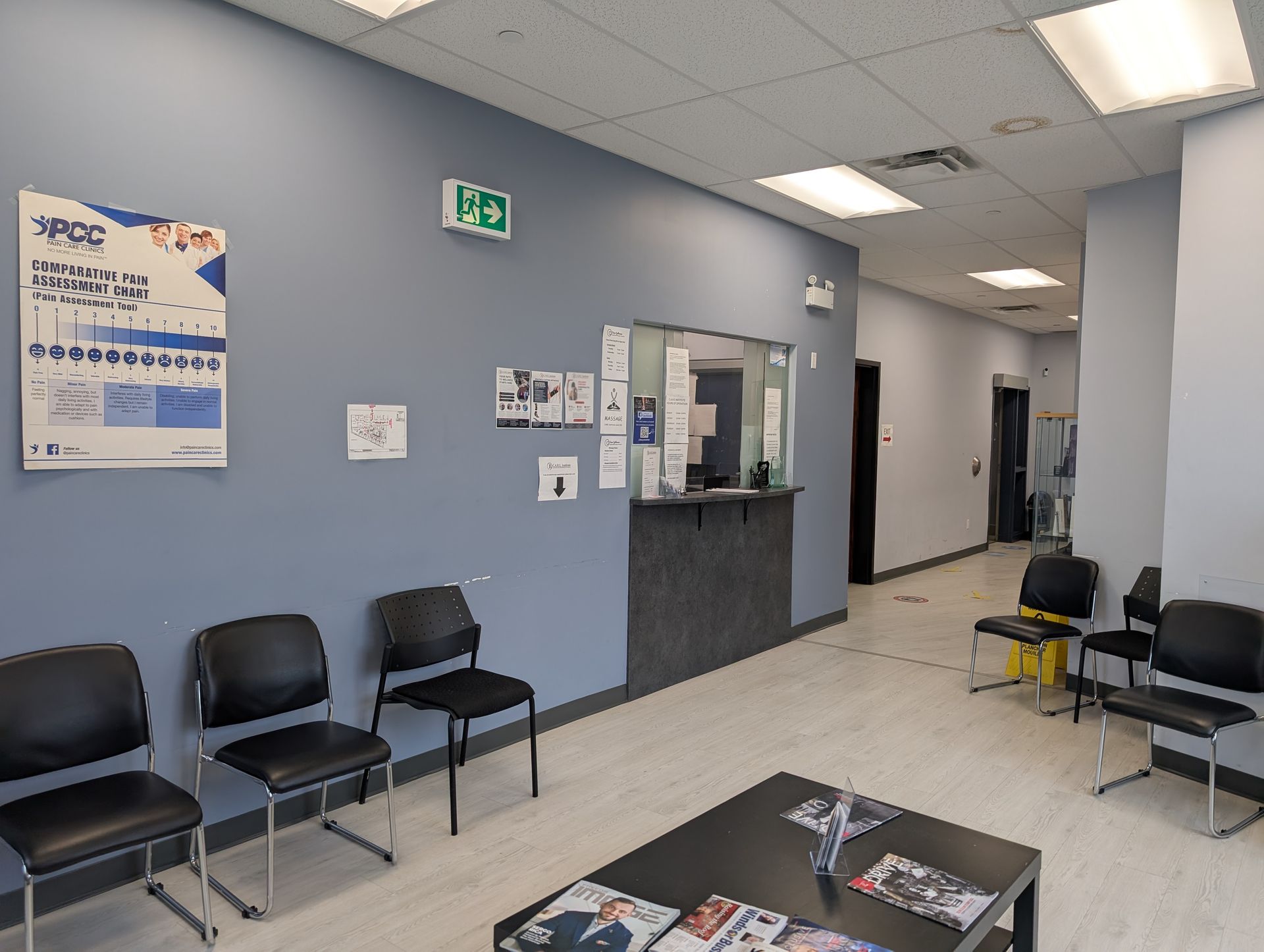 Waiting area with black chairs, gray walls, posters, and a small reception counter in a hallway