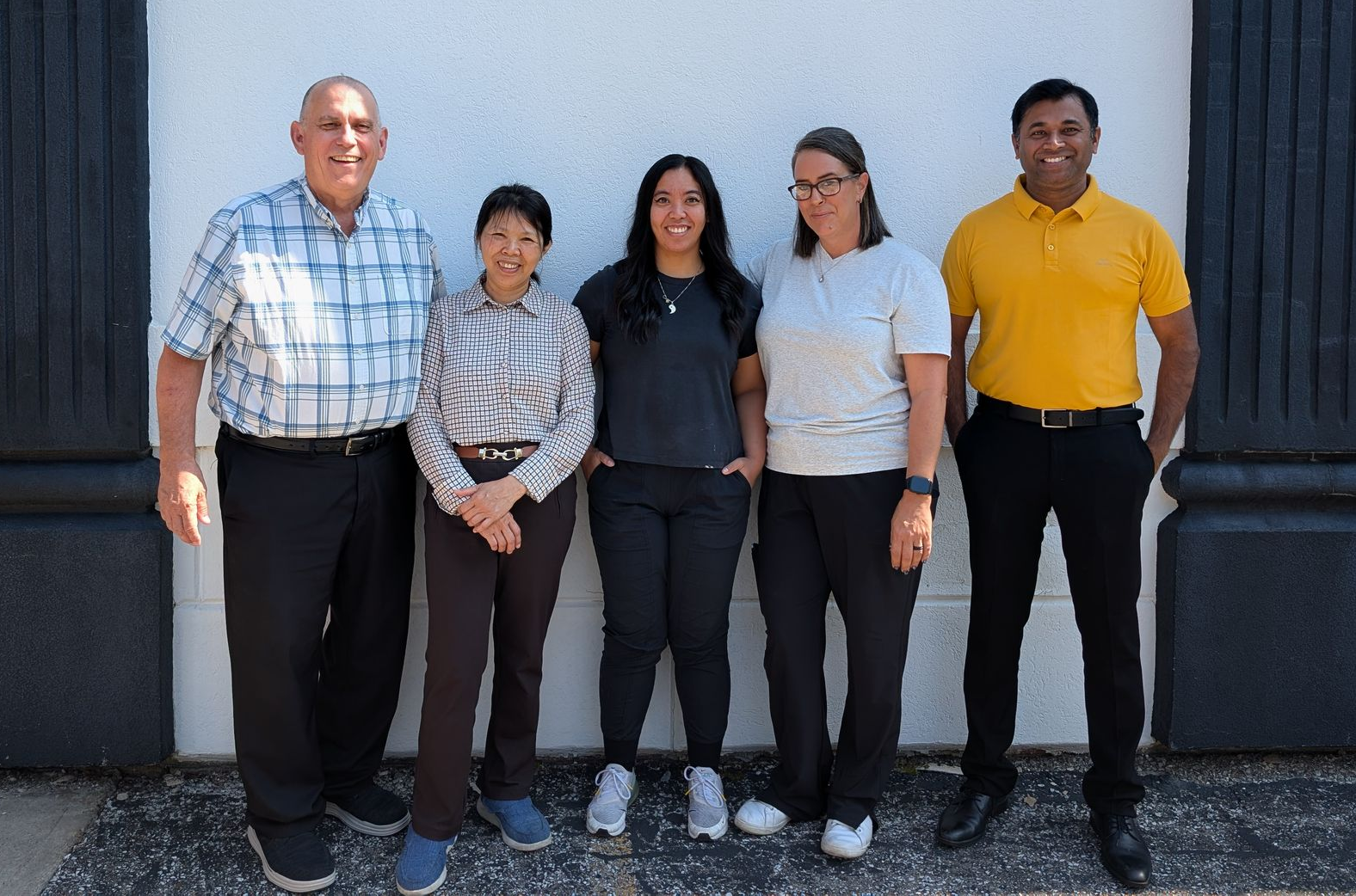 Five people standing together outdoors in front of a building, wearing casual clothes and smiling.