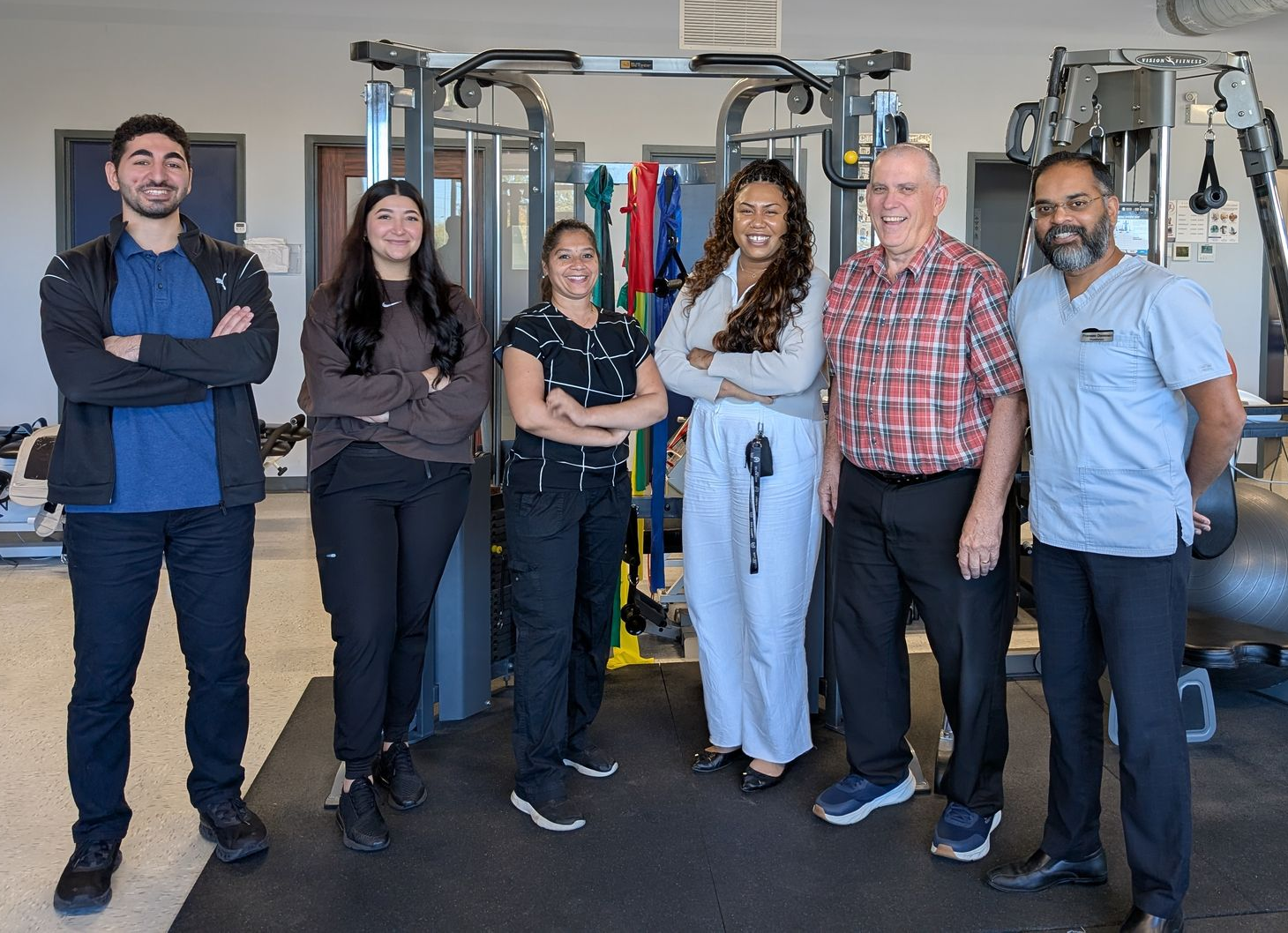 Six people standing in a gym with exercise equipment, posing and smiling.