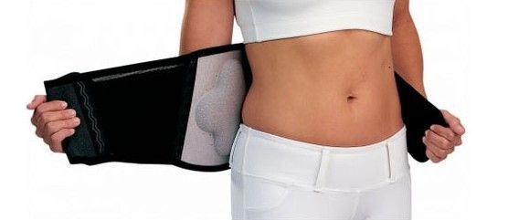 Person wearing a black waist trainer around the midsection, fastening it over a white outfit