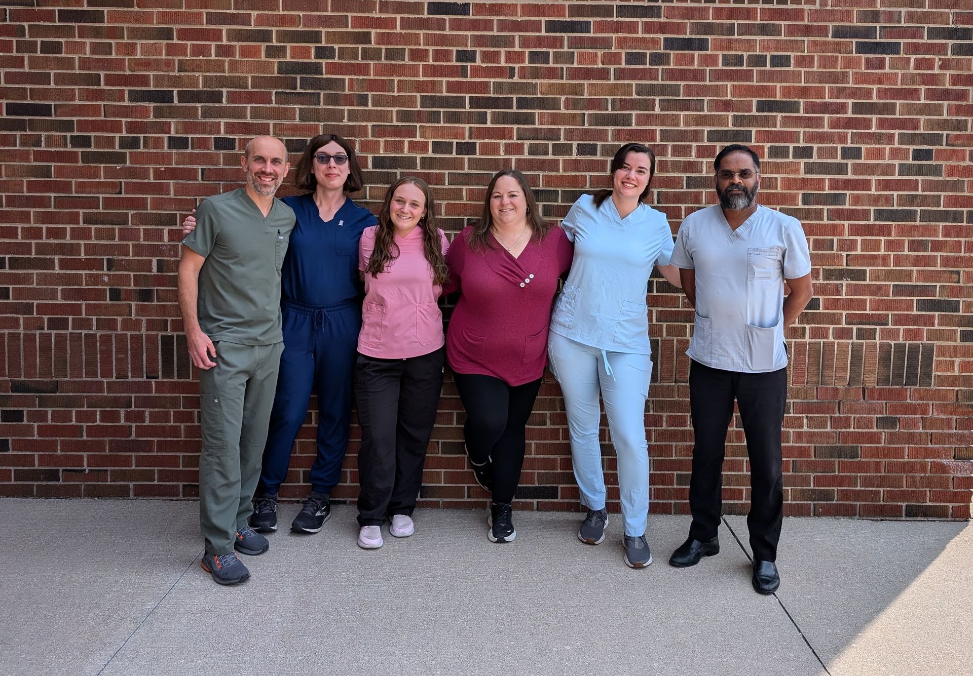 Six people standing together in front of a brick wall, posing outdoors.