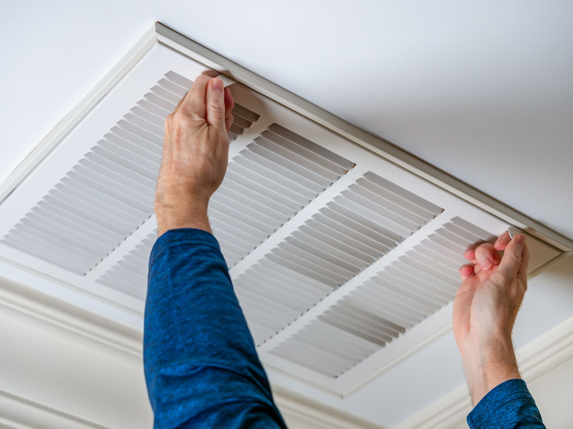 Des mains ajustant un panneau de filtre de ventilation de plafond blanc avec des manchons bleus visibles