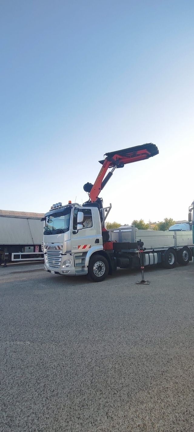 Una gru bianca montata su un camion è parcheggiata su un terreno ghiaioso sotto un cielo azzurro e limpido.